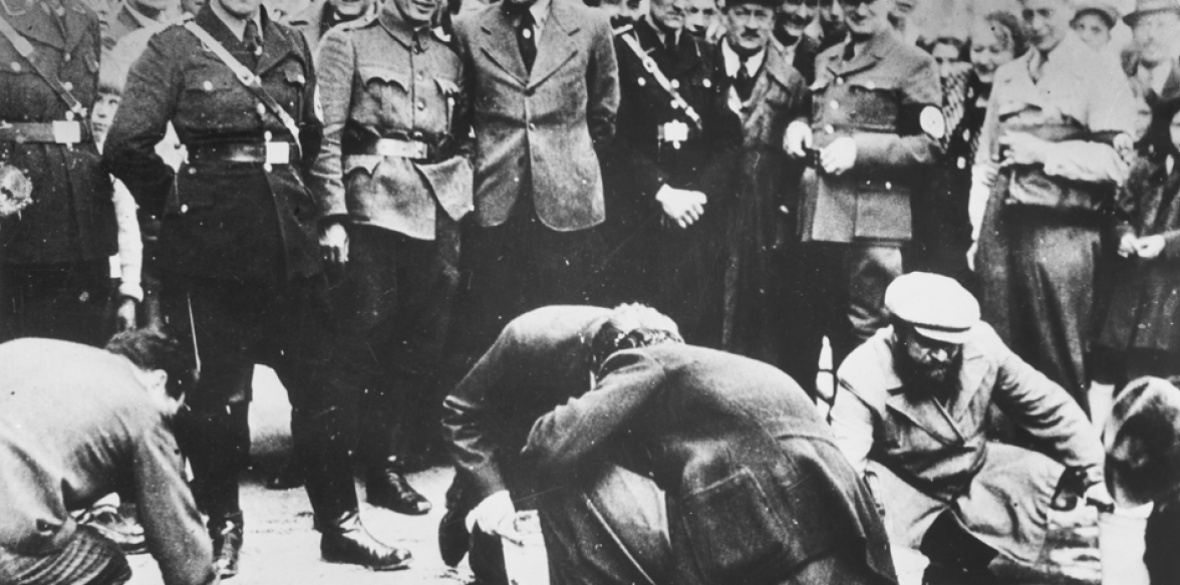 Austrian Nazis and local residents look on as Jews are forced to get on their hands and knees and scrub the pavement in March 1938