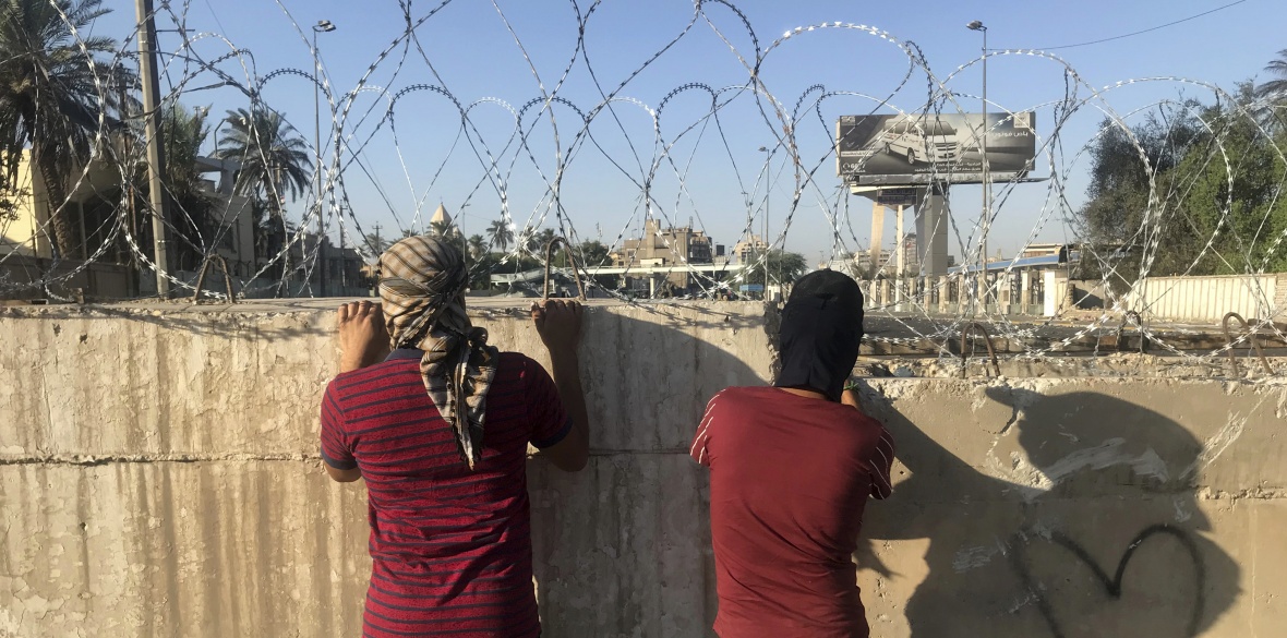 Anti-government protesters look toward the protest site area, blocked with concrete walls by Iraqi security forces in Baghdad