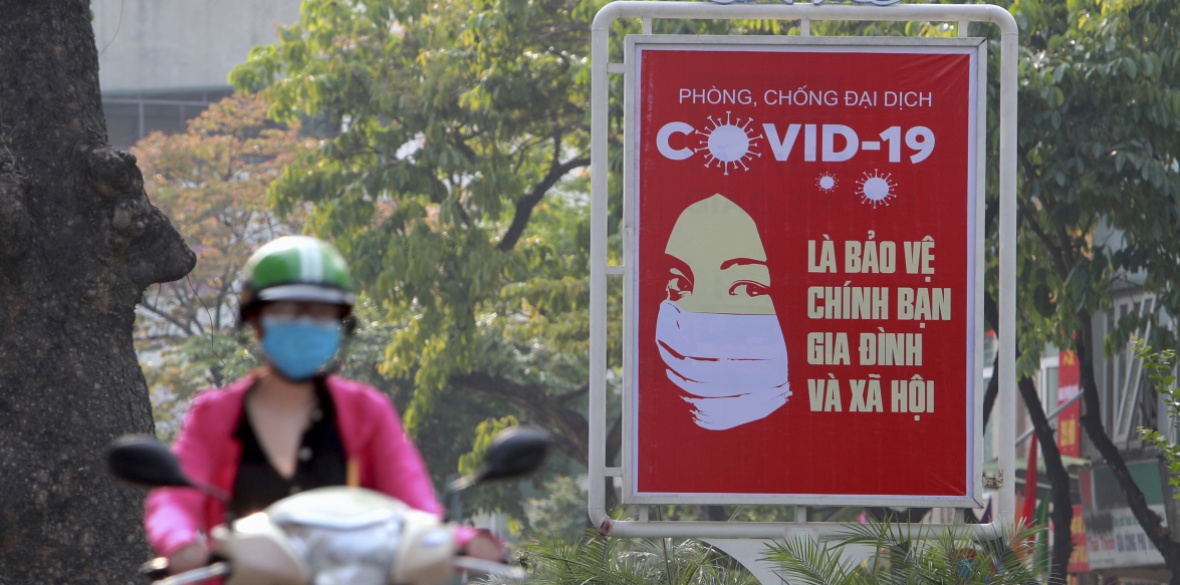 A motorcyclist drives past a poster calling people to take care of their health against coronavirus in Hanoi, Vietnam
