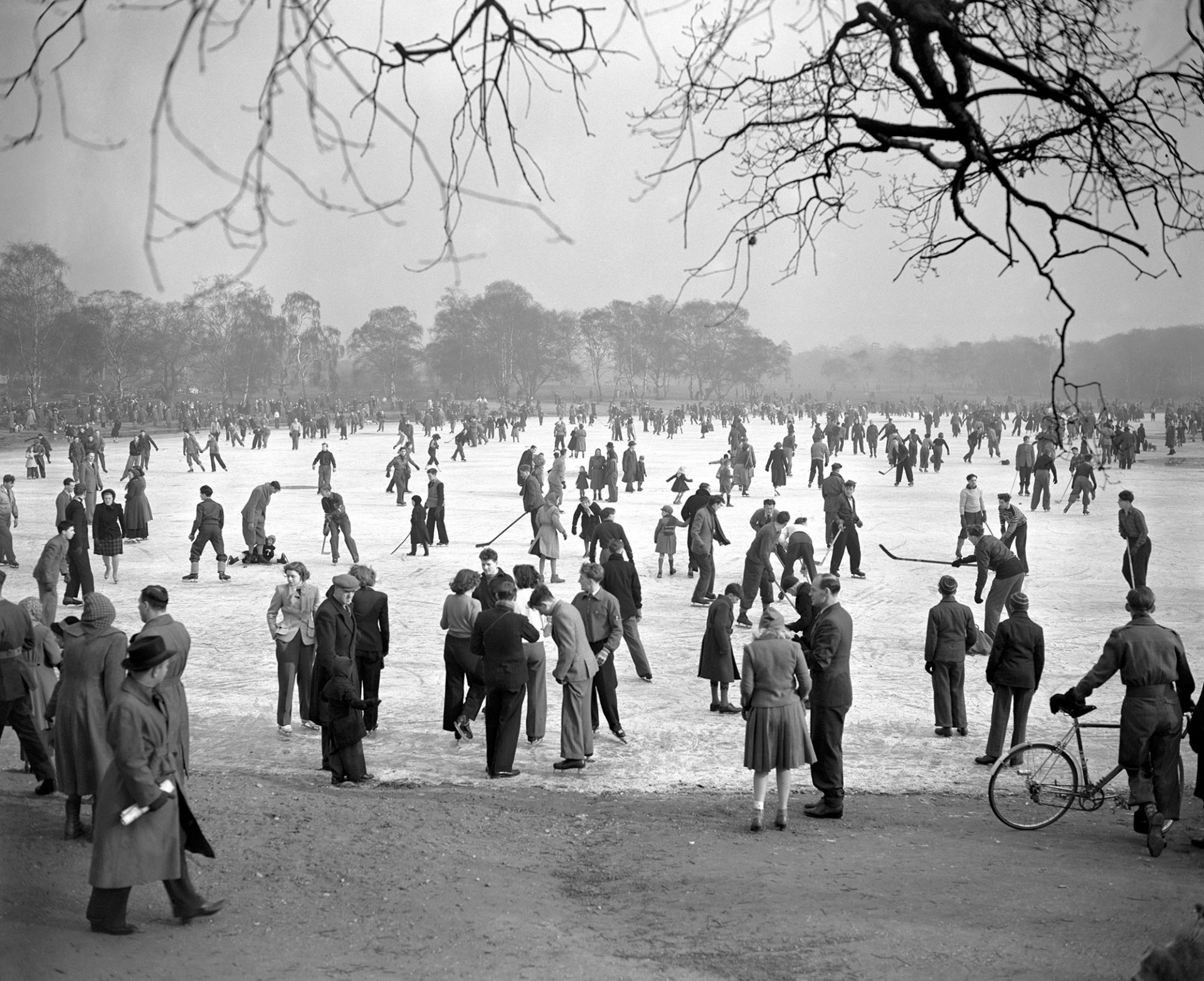 People ice skating and playing ice hockey on the frozen Wimbledon Common Pond, 1950