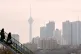 Two women walk across an overpass as Milad telecommunication tower and residential buildings are seen in a high air pollution in Tehran, Iran, December 7, 2025