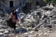 Aida Jleilati, who returned to her village following the announcement of an initial ceasefire agreement between the US and Iran, carries her belongings as she walks on the rubble of her destroyed house in Nabatiyeh town, southern Lebanon, June 16, 2026
