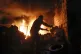 People try to remove car tyres from a car shop on fire after