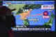 A man walks past a street TV showing a news program on North