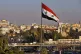A Syrian national flag waves as vehicles move slowly on a br