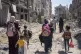 Palestinian women and their children walk though destruction