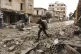 A man carries his belongings through a street destroyed in r
