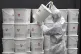 A worker in protective gear stacks plastic buckets containin