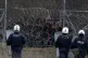 Greek riot police guard as migrants stand on a fence as they