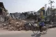 A local man rides a bicycle past a damaged building in the a