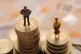 Plastic models of a man and woman stand on a pile of coins a